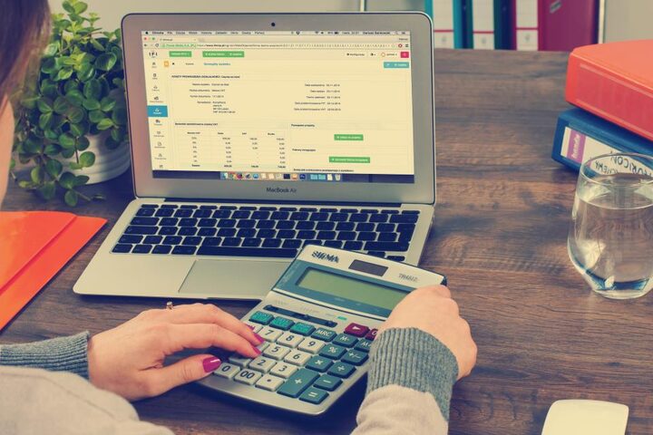Hands working a calculator beside a ledger on screen